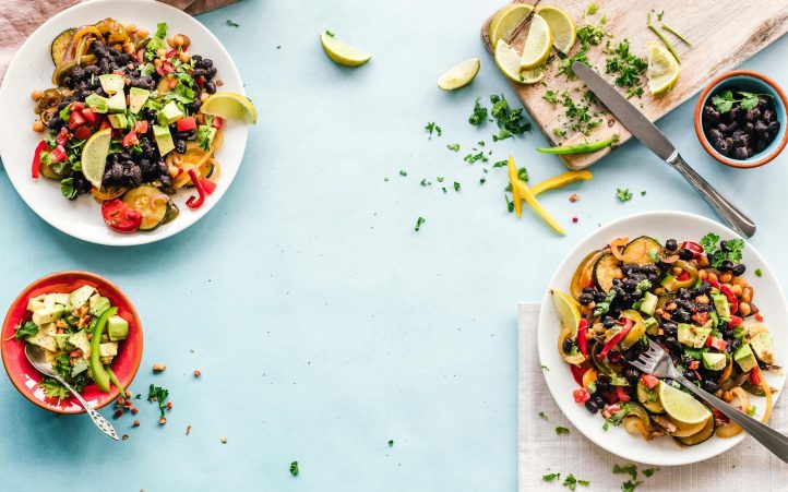 Colorful Mexican salad with avocado, black beans, and lime on a light blue surface.