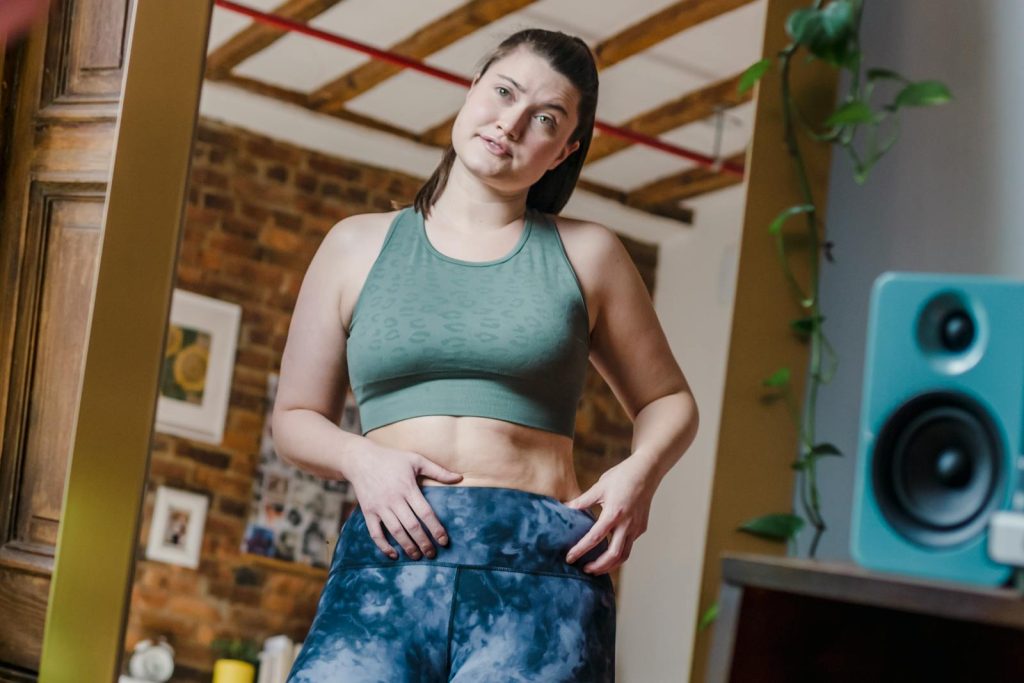 Woman confidently poses in activewear, embracing body positivity in a cozy indoor setting.